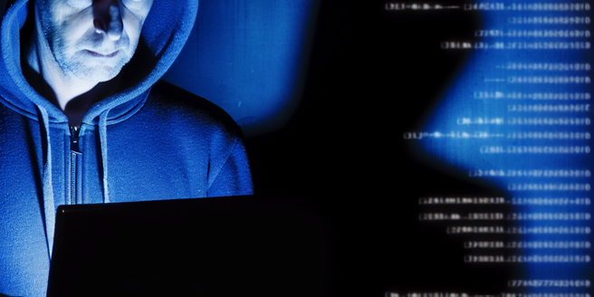 A man in a hoodie in the dim-light symbolizing a hacker breaking into a database